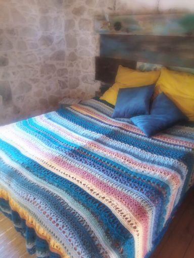 Letto con copriletto a righe colorate e cuscini blu su sfondo di pietra.